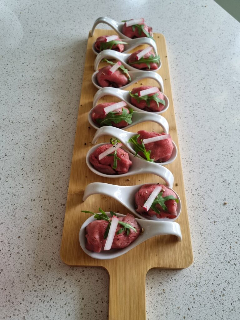Acht elegante witte lepels met rood vlees en rucola